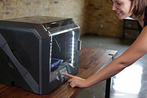 Person operating a 3D printer on a wooden table