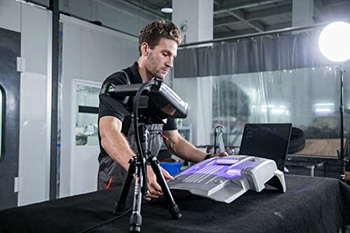 Technician using a 3D scanner on a table with a laptop nearby.